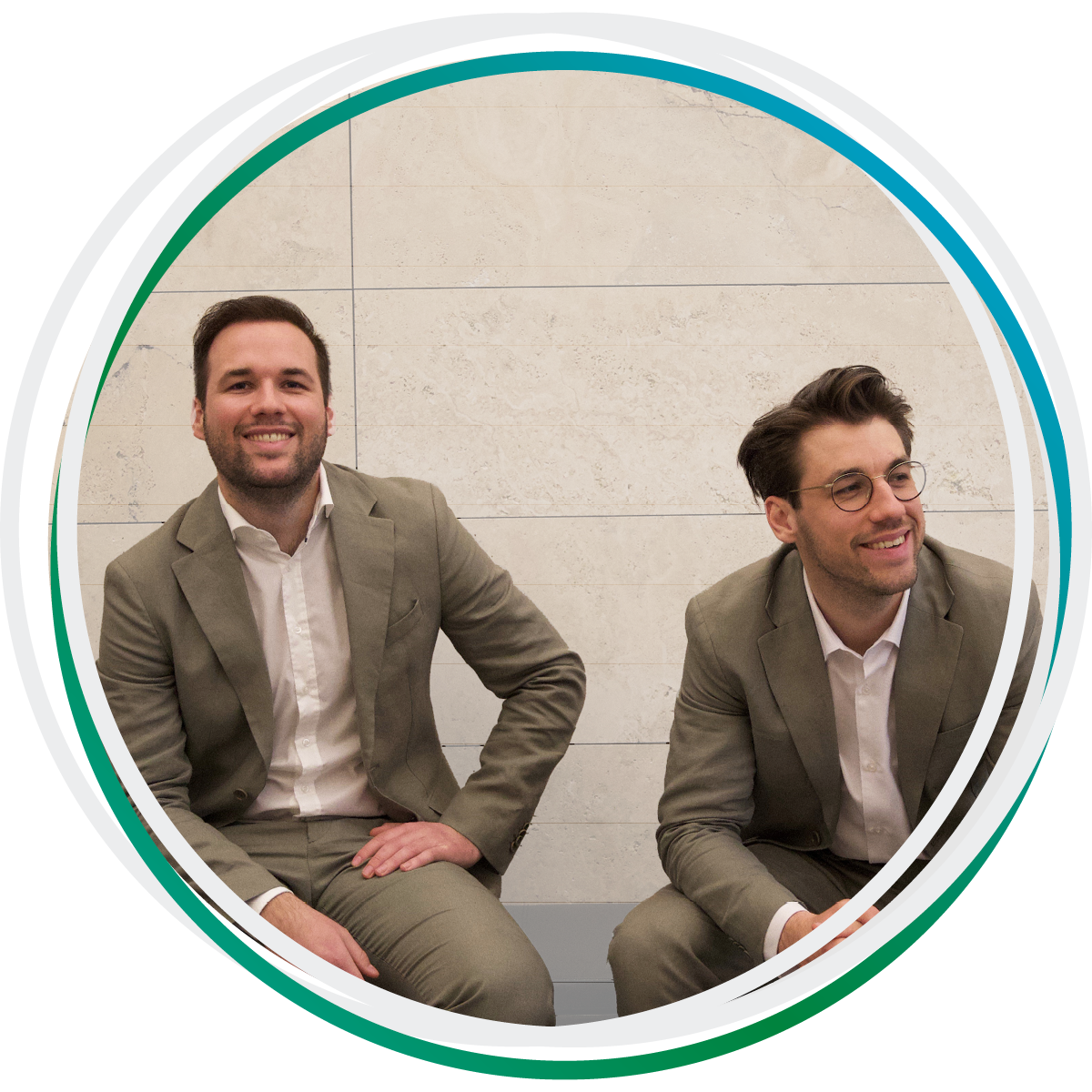 Die Rechtsanwälte Niklas und Lukas Hufeld sitzen vor einer Mauer und lächeln. Beide tragen einen beigen Anzug.