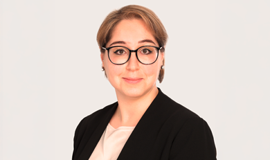 Özgün Habenstein, Teamleader Claims Commercial Lines bei Hiscox, trägt einen schwarzen Blazer und eine schwarze Brille und blickt lächelnd in die Kamera