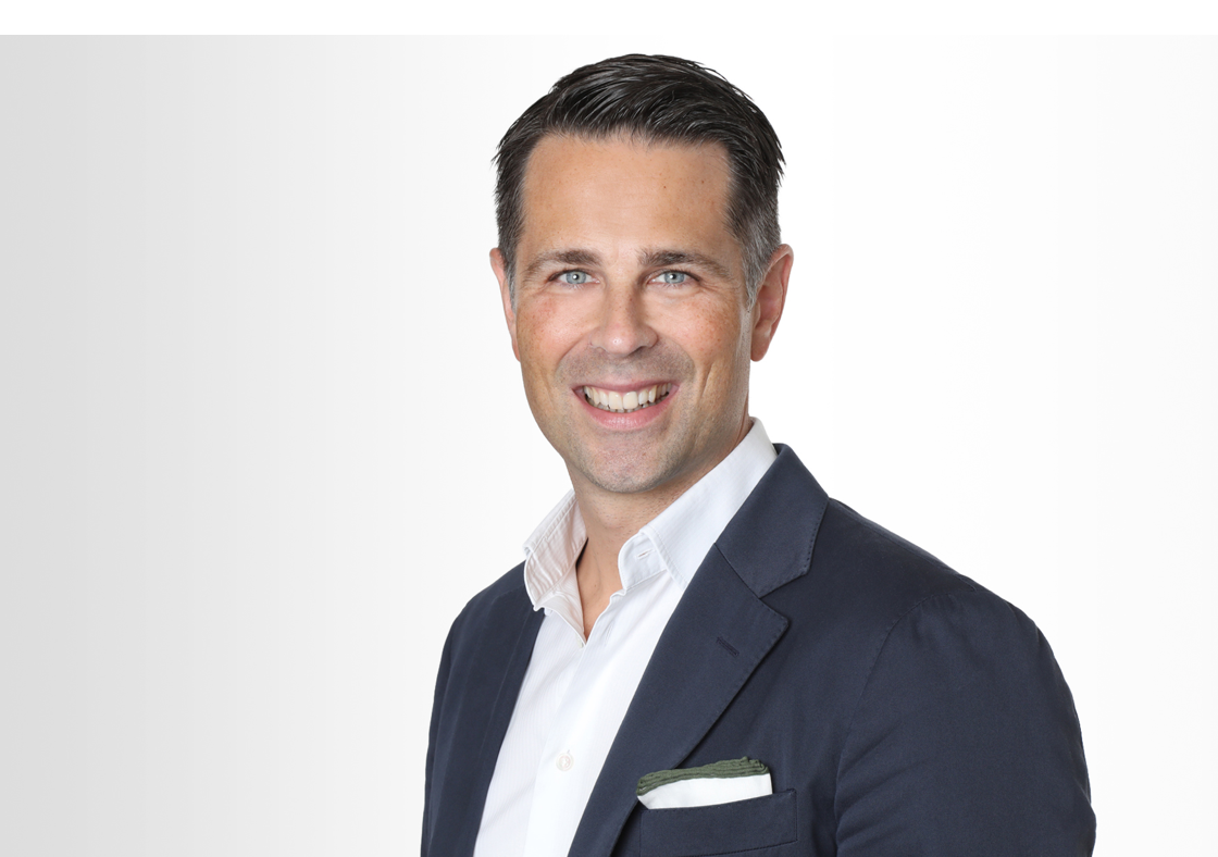 Der Deutschland-Chef von Hiscox Tim Bethge trägt ein dunkles Sakko und weißes Hemd und lächelt in die Kamera