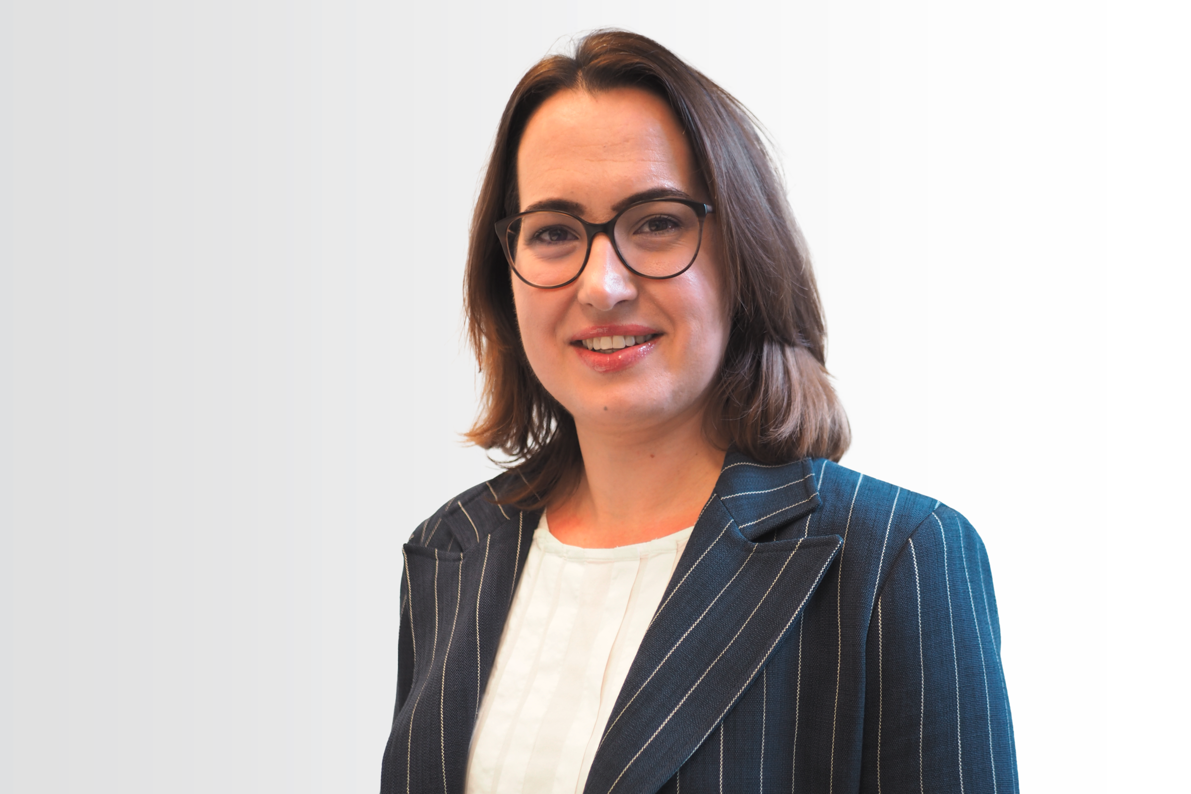 Die HR-Chefin Claudia Heckelmann trägt lange braune Haare, eine Brille, ein Jackett zur weißen Bluse und lächelt in die Kamera.