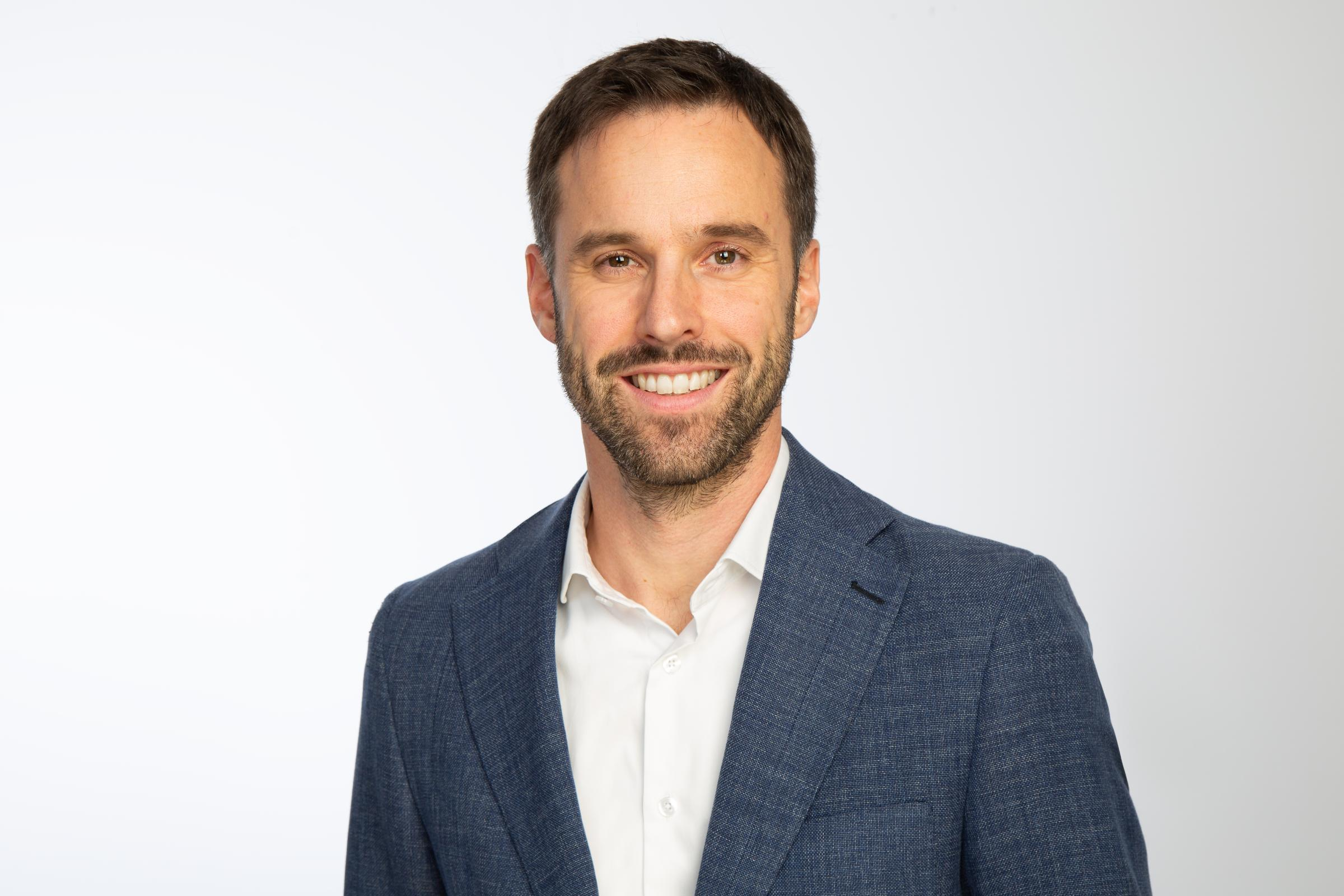 Franz Kupfer ist Product Head Professional Indemnity, D&O bei Hiscox Sa. Er trägt einen dunkelblauen Anzug mit weißem Hemd drunter.