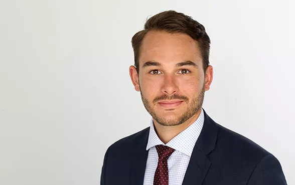Moritz Assenmacher trägt ein dunkles Sakko, ein weißes Hemd mit Karomuster und eine rote Krawatte mit kleinen weißen Punkten.