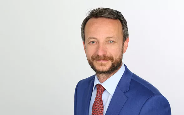 Markus Klopfer, vom Management Team, trägt ein blaues Sakko, ein weißes Hemd und eine rote Krawatte.