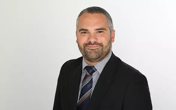 richard weber, der teil des hiscox management team ist, trägt einem dunklen Anzug mit weißem Hemd und blau-schwarz gestreifter Krawatte.