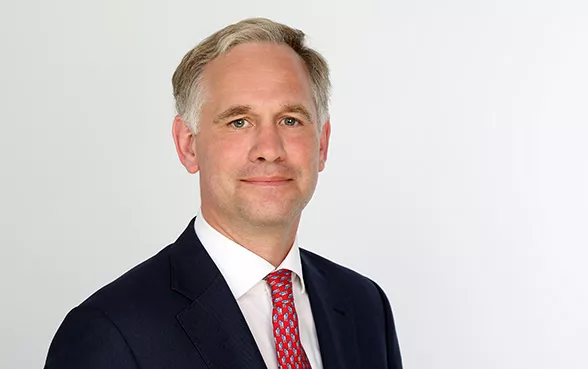 Wolf von Buchwaldt, Director Broker Sales, in Anzug und Krawatte steht vor einem weißen Hintergrund und lächelt leicht.