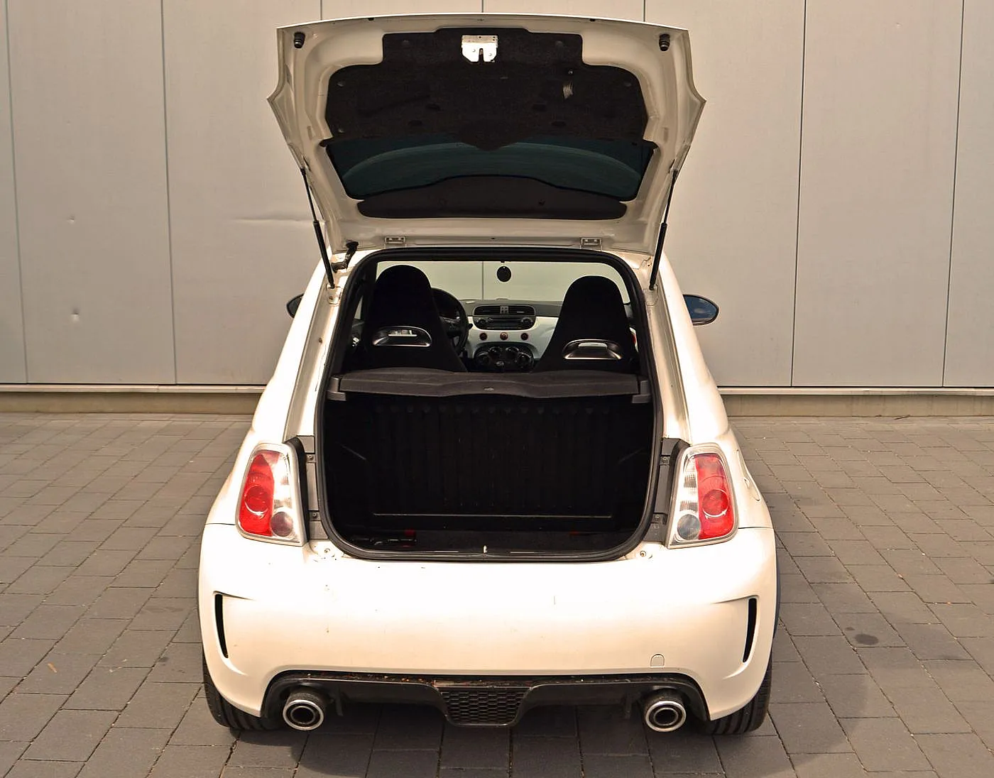 Weißer Abarth 500 steht parkend vor einer grauen Wand mit Blick in den offenen Kofferraum.