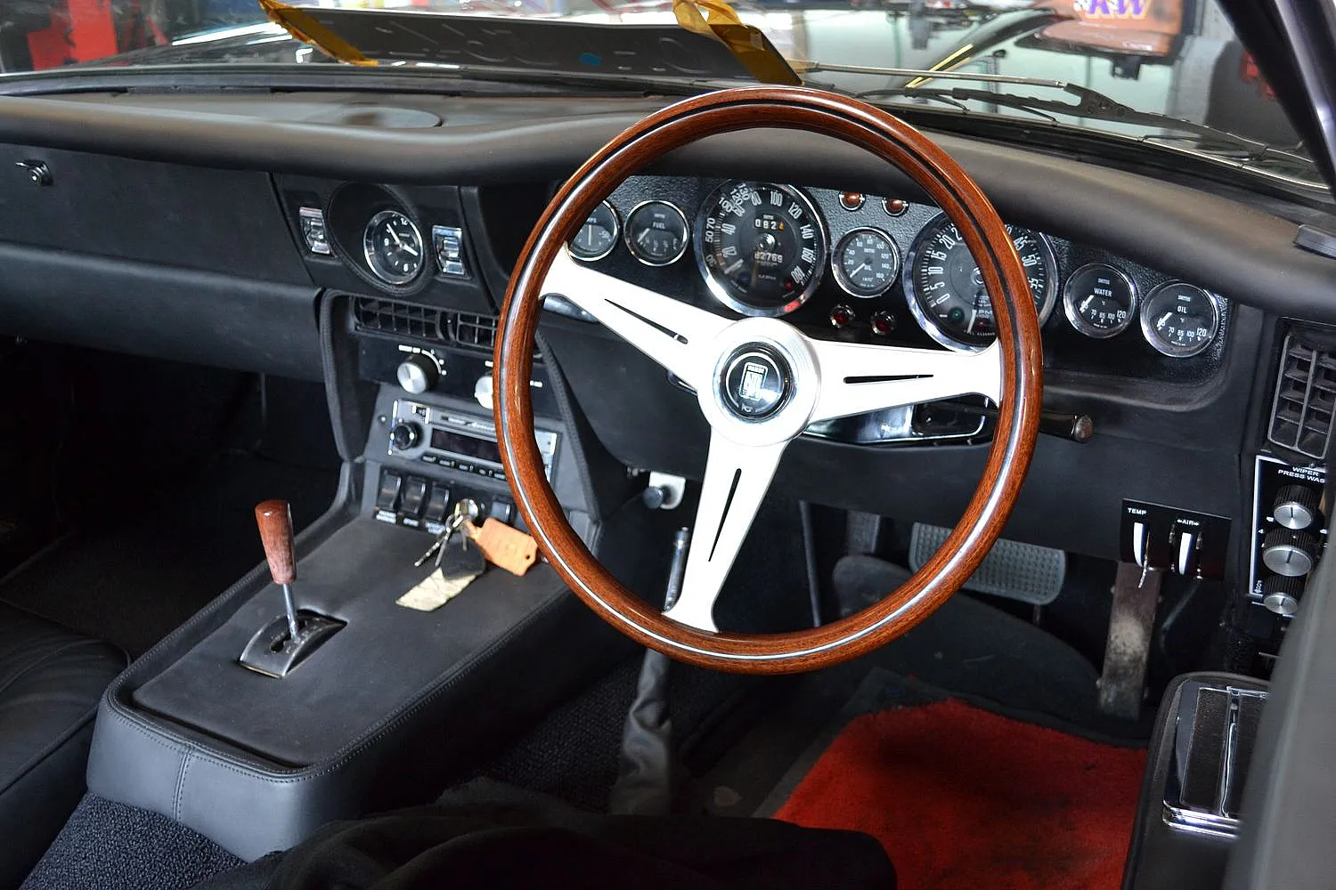 Das Innere eines klassischen Autos mit einem Holzlenkrad und mehreren Anzeigen auf dem Armaturenbrett. Der Schalthebel ist links vom Lenkrad.