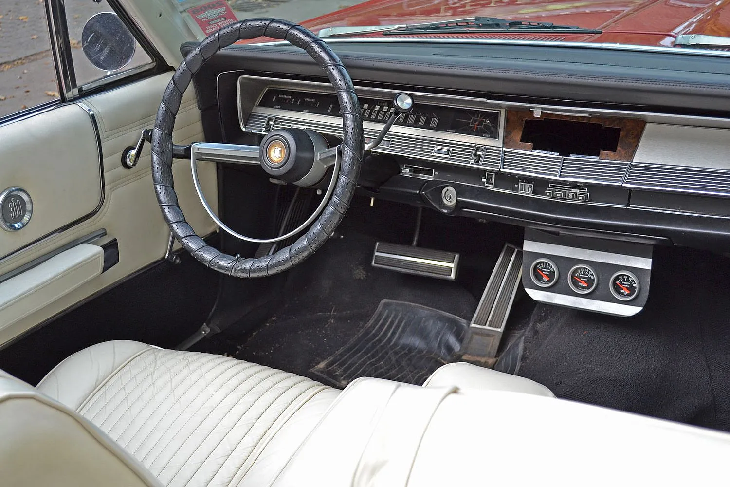 Das Innere eines klassischen Autos mit einem schwarzen Lenkrad, weißer Lederausstattung und einem Armaturenbrett mit verschiedenen Instrumenten.