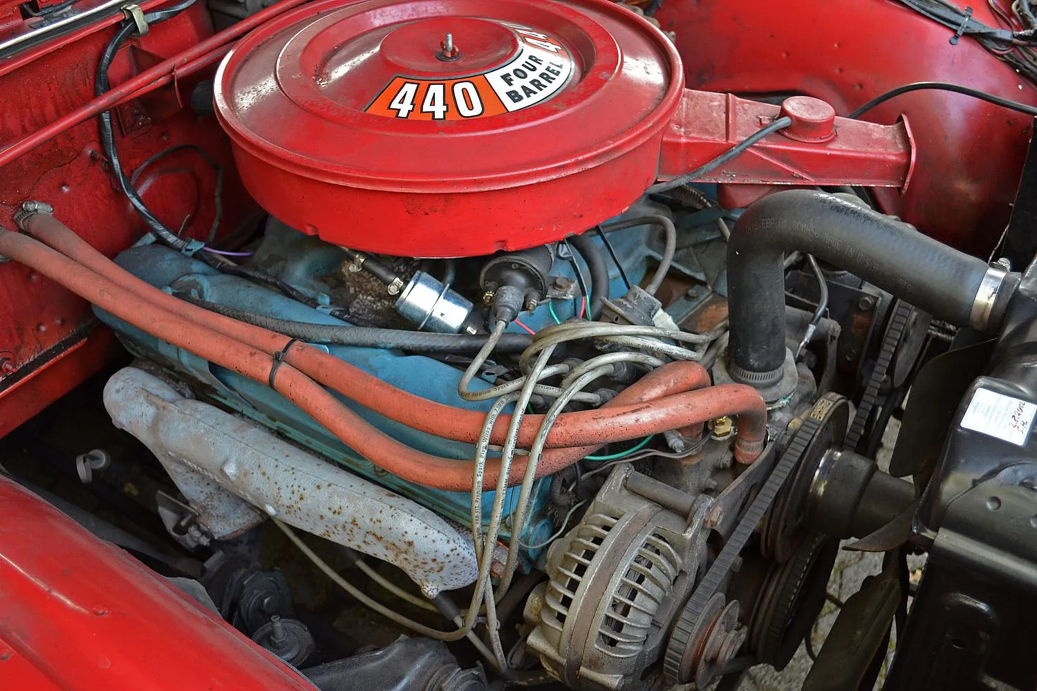 Ein roter Motorraum eines Autos mit einem großen Luftfiltergehäuse, auf dem "440 Four Barrel" steht. Mehrere Kabel und Schläuche sind um den Motor herum sichtbar