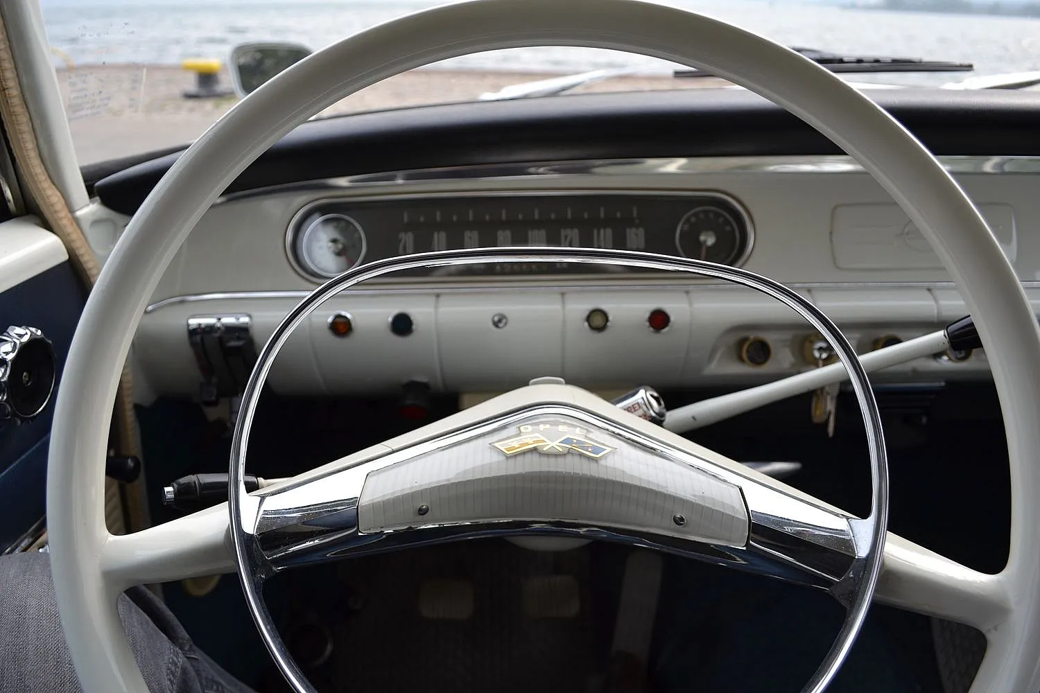 Innenraum eines Oldtimers mit großem Lenkrad, analogem Tachometer und verschiedenen Knöpfen und Schaltern.