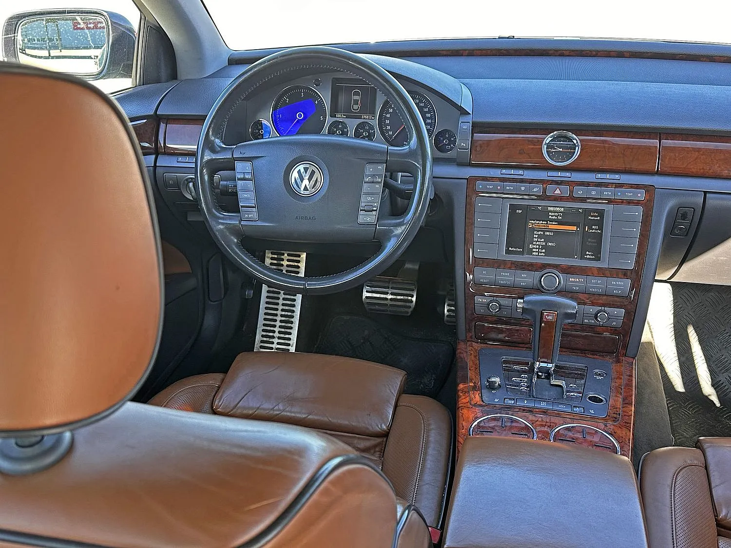 Luxuriöses Interieur mit hellbraunen Ledersitzen, einem Volkswagen Phaeton Individual Lenkrad und einem holzgetäfelten Armaturenbrett mit Touchscreen und Analoguhr.