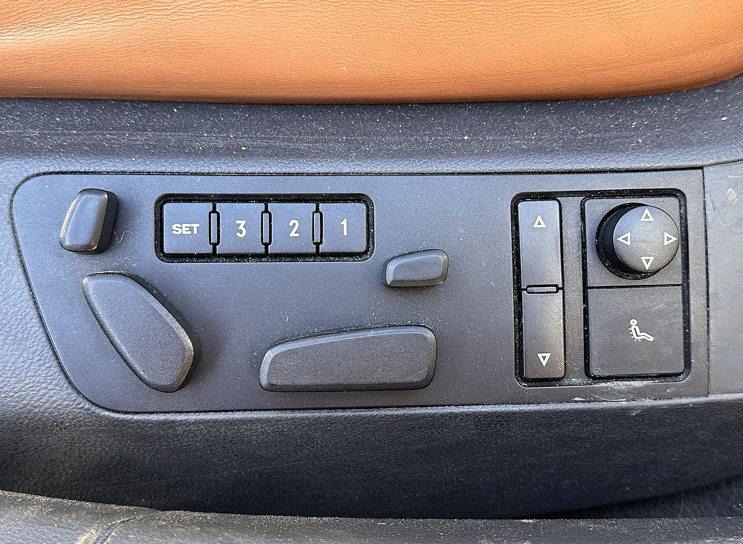 Nahaufnahme eines Bedienfelds für die Autositzverstellung mit Tasten für die Einstellung der Positionen 1-3 und Hebeln für die Einstellung des Sitzwinkels. Mattes Schwarz mit strukturierter Oberfläche.