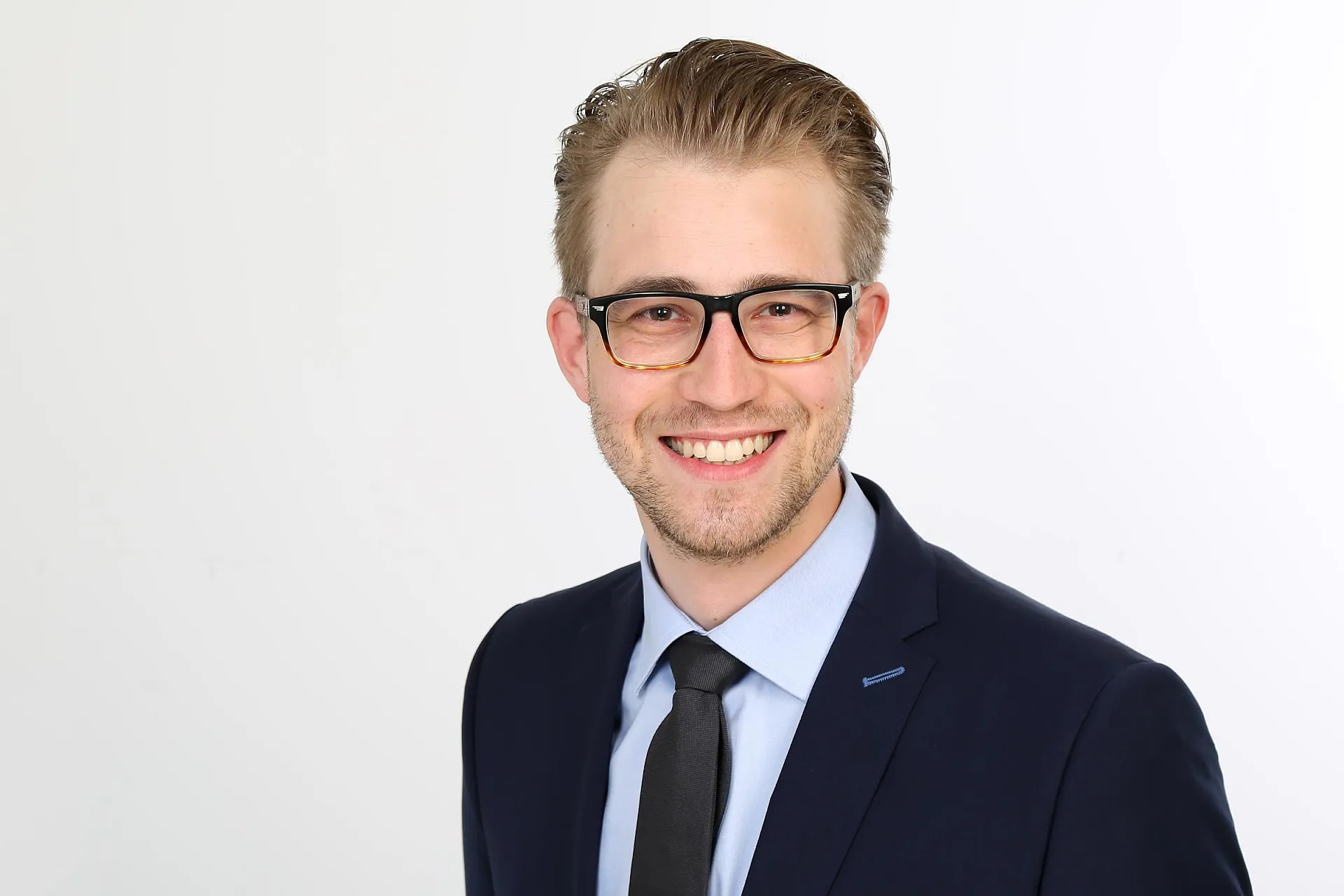 Hiscox Underwriter Bastian Lutz trägt Anzug und Krawatte und lächelt in die Kamera.