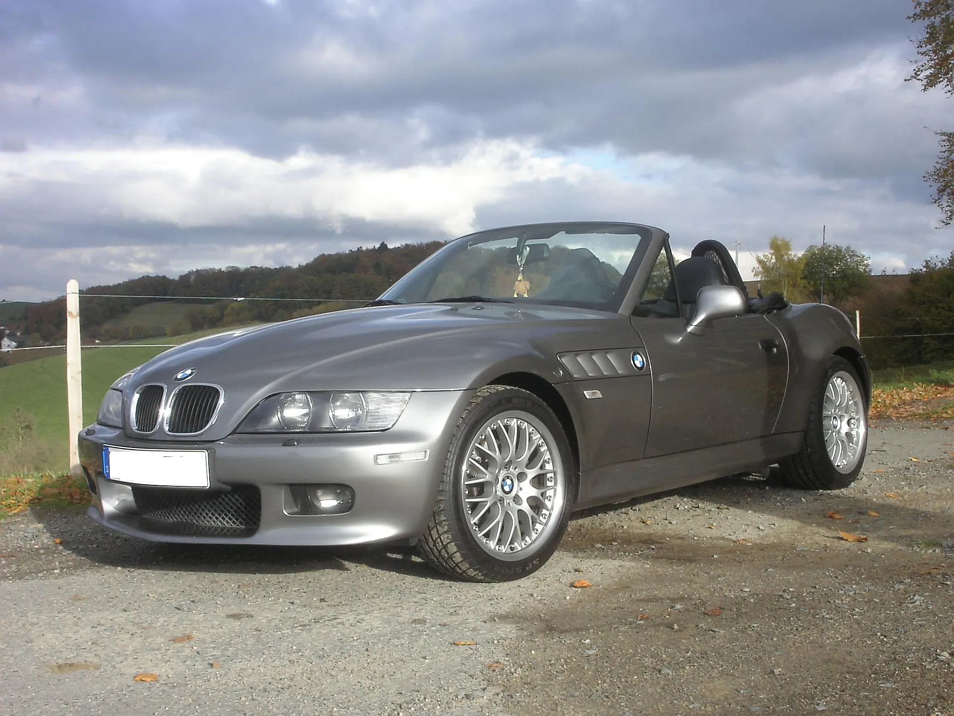 Silberner BMW Z3 mit offenem Verdeck parkt auf einem Feldweg. Man sieht das Front- und Seitenprofil des neuen Oldtimers.