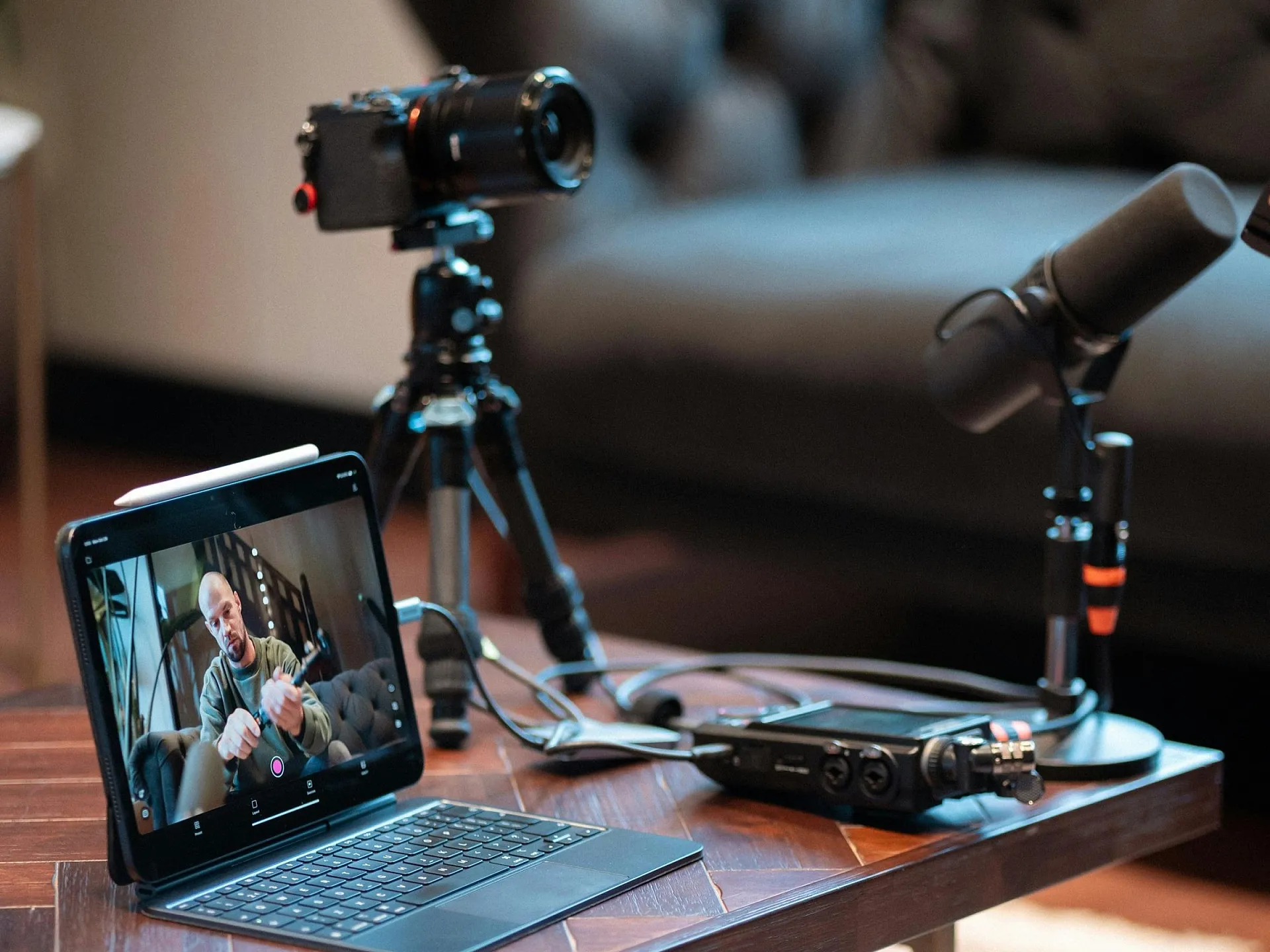 Ein Podcast-Setup zu Hause auf einem Holztisch, bestehend aus einem Laptop, auf dem ein Interview zu sehen ist, einer Kamera auf einem Stativ, Mikrofonen und Audiogeräten. Gemütliche Atmosphäre.