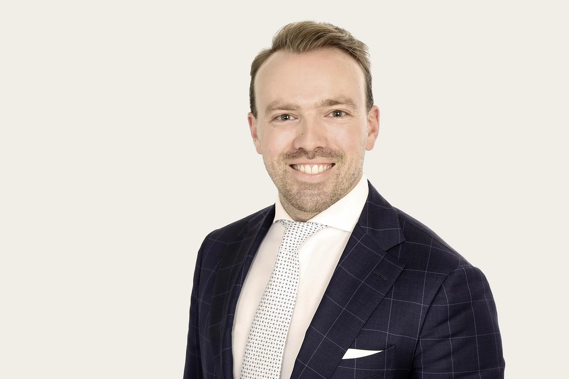 Jakob Esswein trägt einem dunkelblauen karierten Anzug, einem weißen Hemd und einer weißen Krawatte mit kleinen schwarzen Punkten.