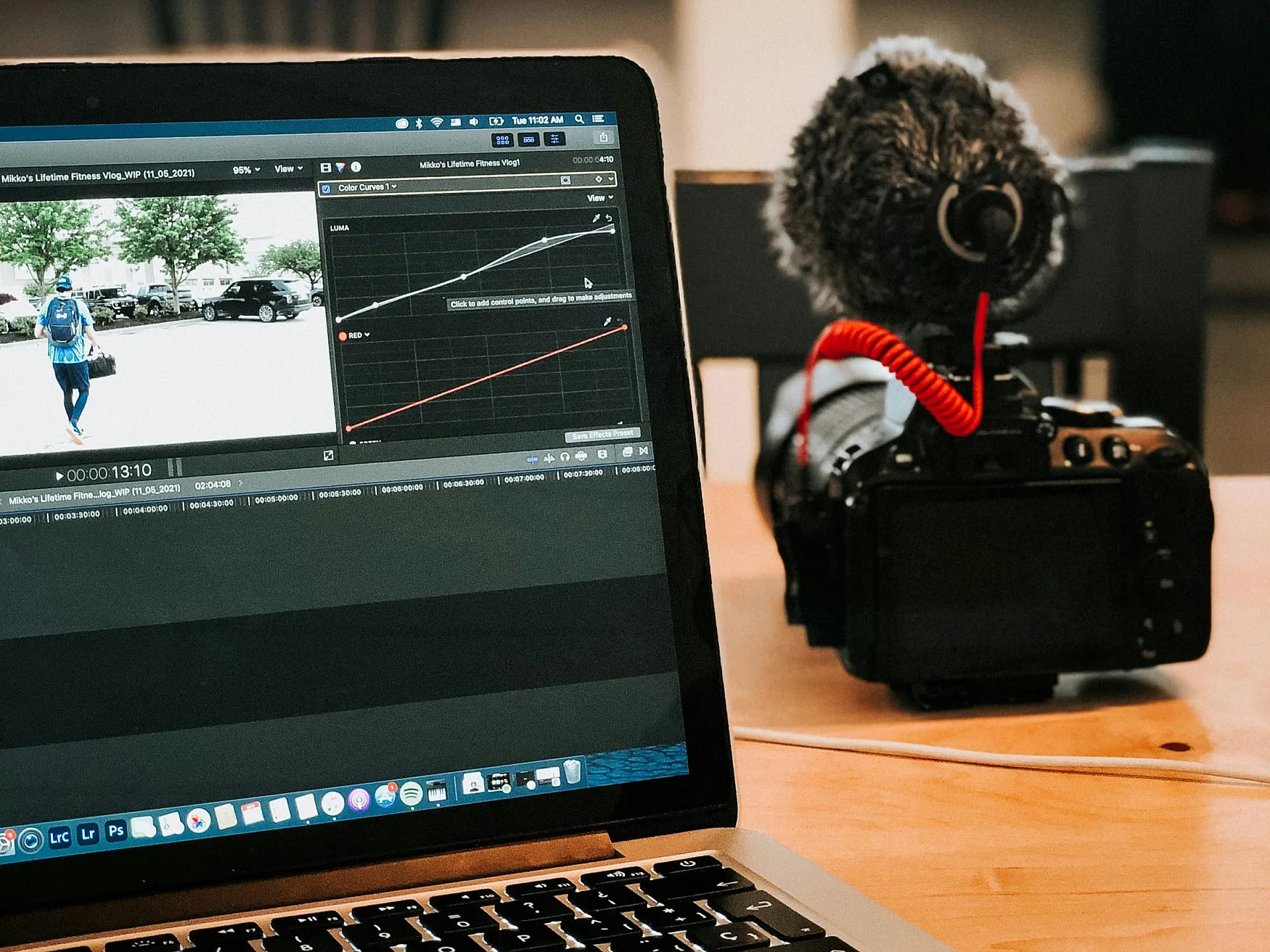 Auf einem Holztisch steht ein Laptop, auf dem eine Videobearbeitungssoftware läuft, daneben eine Kamera mit Mikrofon. Die Szene vermittelt den Eindruck eines kreativen Arbeitsbereichs.