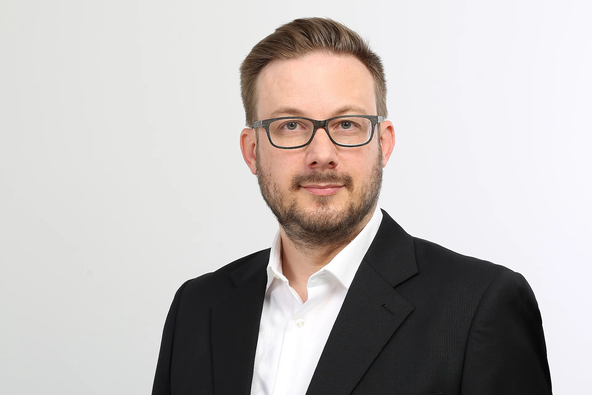 Leo Molatore, ein Mann in einem schwarzen Anzug und weißem Hemd, steht vor einem weißen Hintergrund.