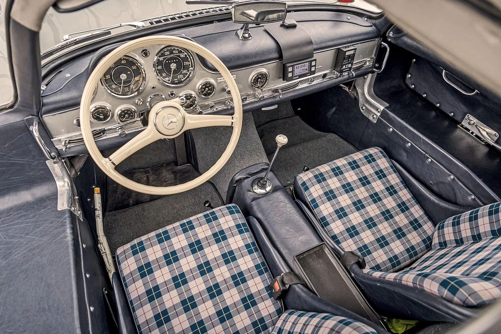 Vorderer Innenraum des mercedes Benz 300 SL mit Blick auf die karierten Vordersitze und das weiße Lenkrad