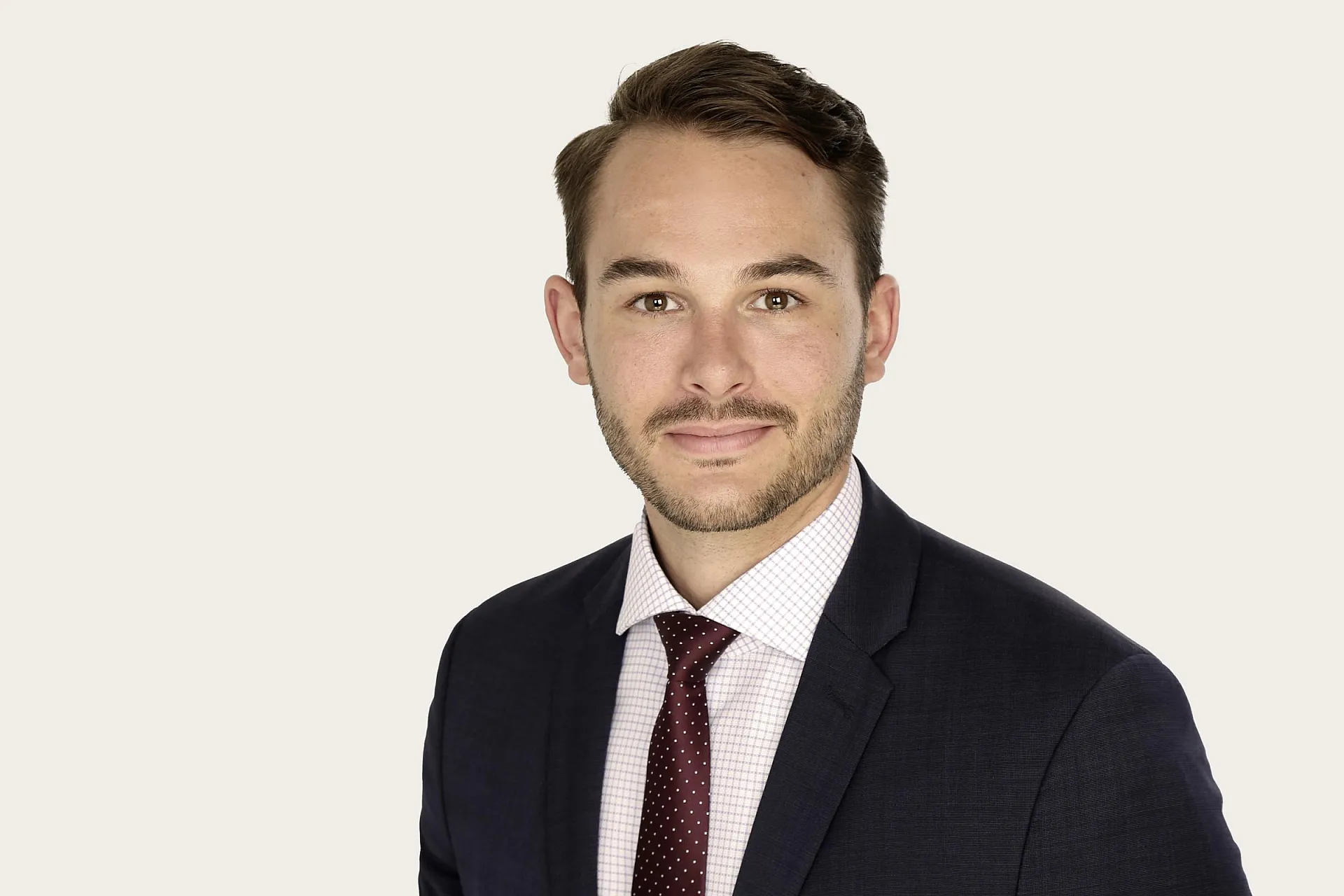 Moritz Assenmacher trägt ein dunkles Sakko, ein weißes Hemd mit Karomuster und eine rote Krawatte mit kleinen weißen Punkten.