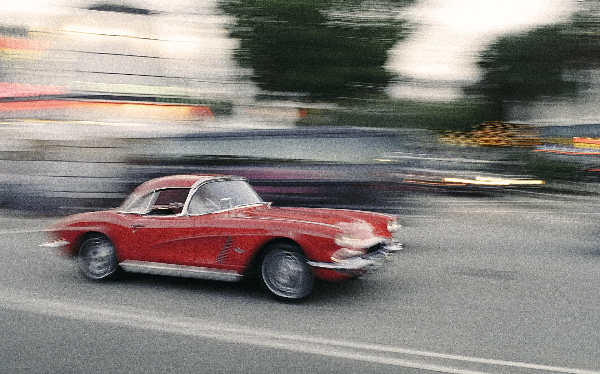 Ein rotes Vintage-Auto, wahrscheinlich ein klassischer Chevrolet Corvette, fährt mit hoher Geschwindigkeit auf einer Straße.