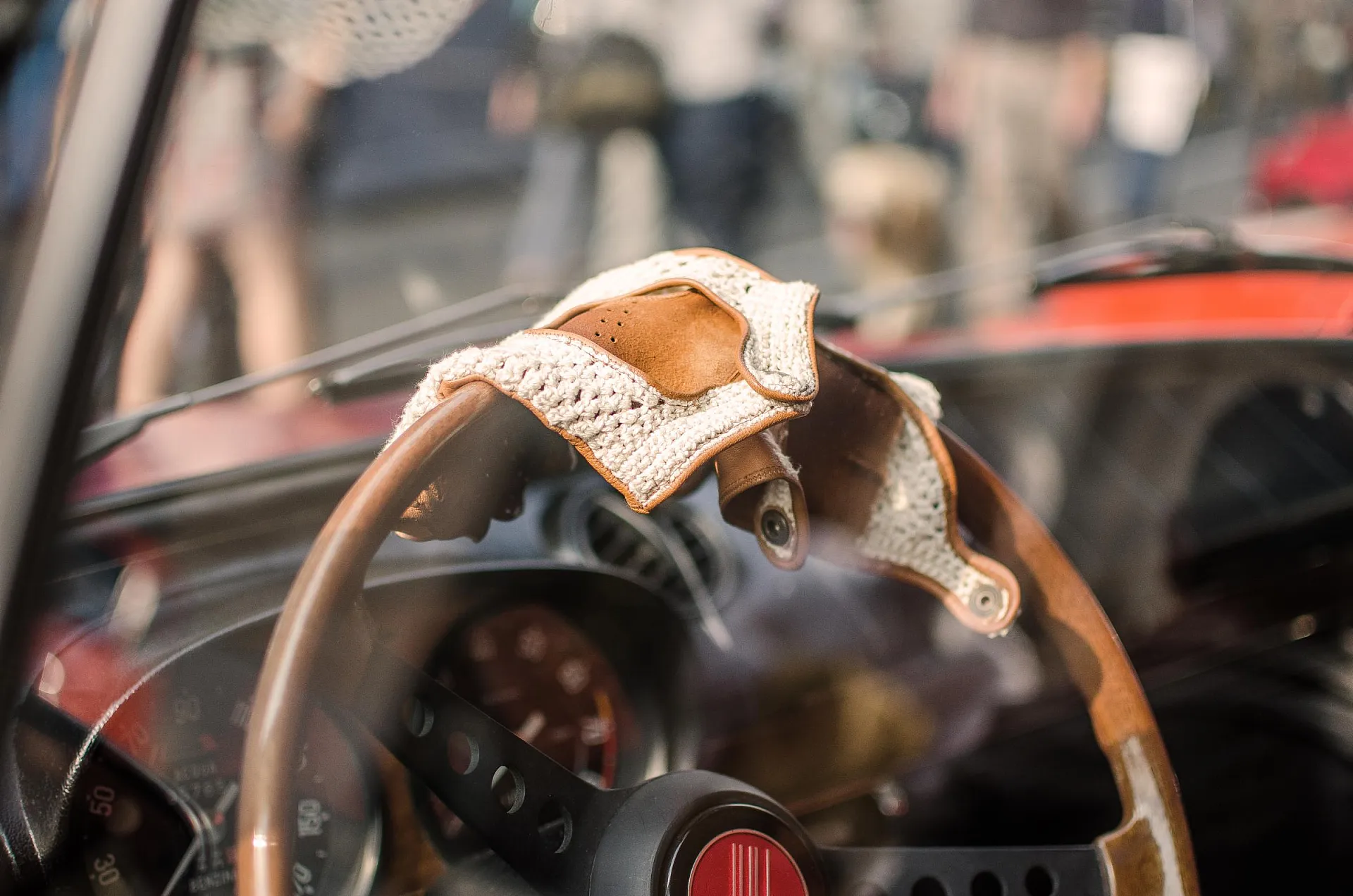 Ein Nahaufnahme des Lenkrads eines klassischen Autos mit darauf drapierten Vintage-Fahrerhandschuhen aus Leder und gehäkeltem Stoff.