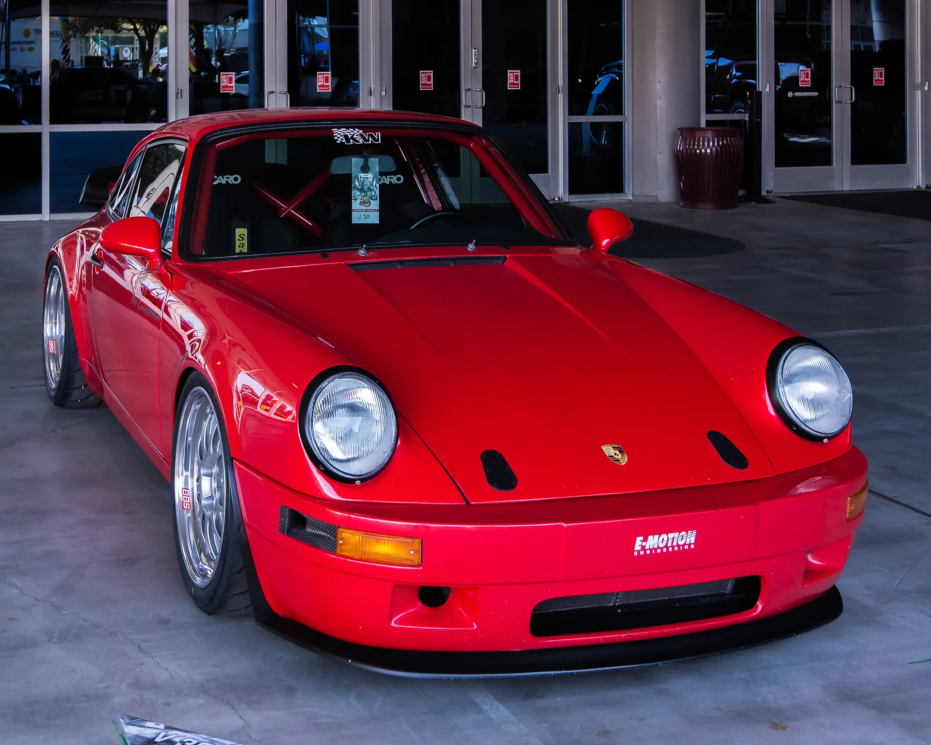 Parkender roter Porsche Carrera 911 Turbo steht vor einem Office-Gebäude. Der Oldtimer parkt schräg seitlich, sodass Seite und Front sichtbar sind.