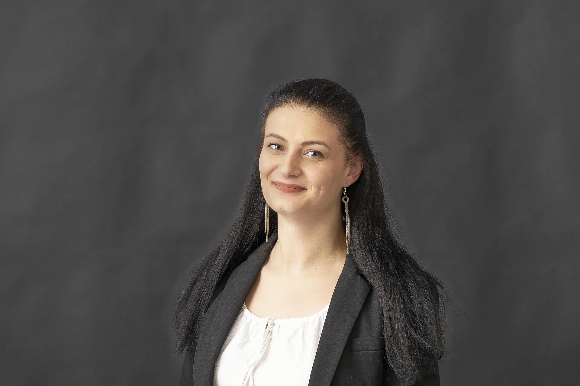 Selina Ziegler Carl Rieck, eine Frau mit langen schwarzen Haaren, trägt einen schwarzen Blazer über einem weißen Oberteil.