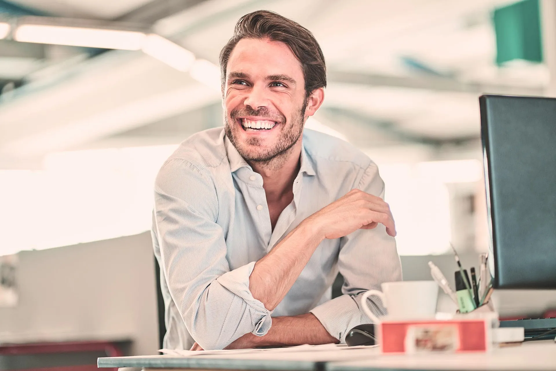 Vermögensschadenhaftpflichtversicherung von Hiscox: Lächelnder Geschäftsmann im Büro: Positive Arbeitsatmosphäre und Motivation am Arbeitsplatz