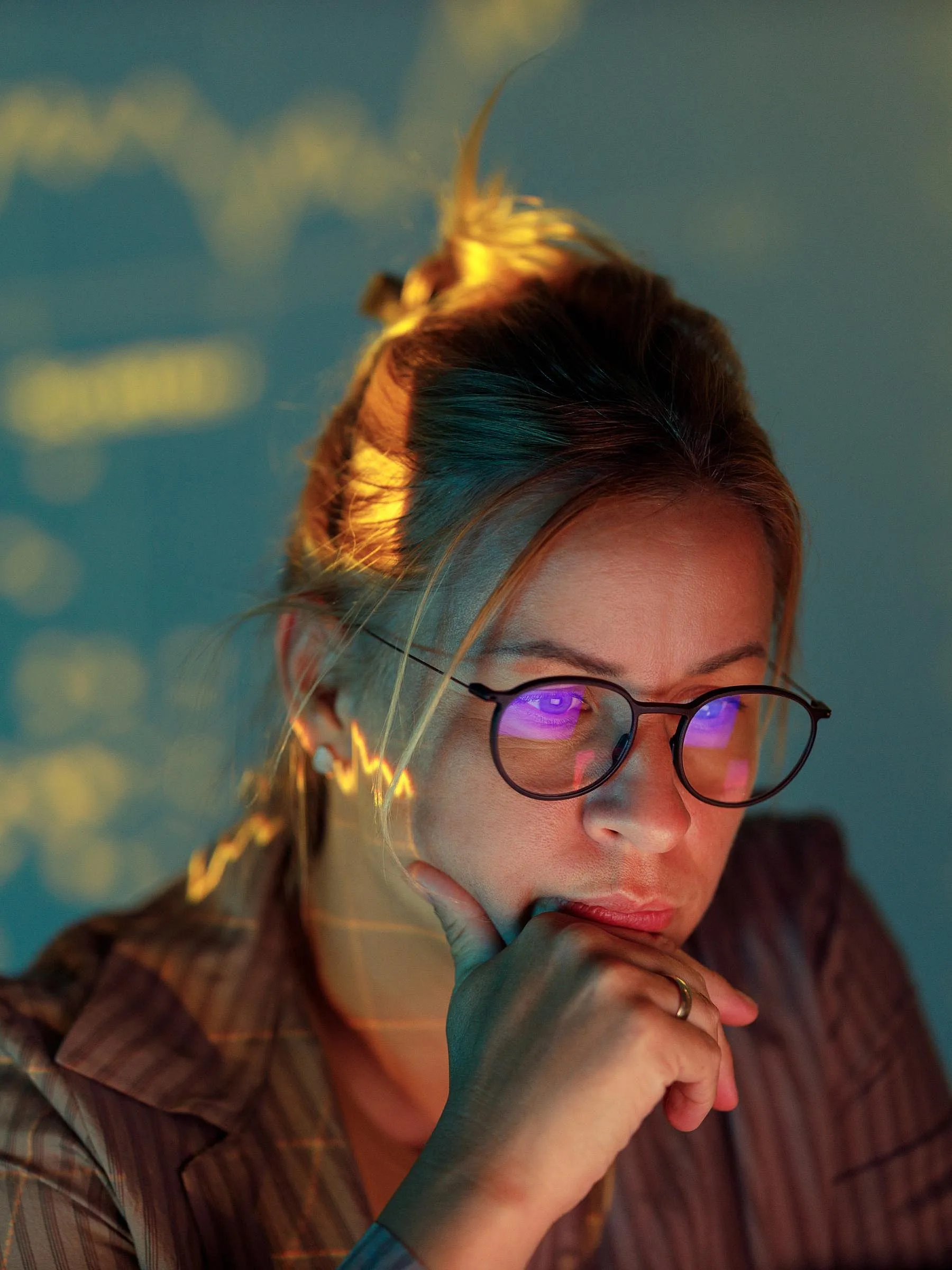 Eine Frau mit Brille blickt konzentriert auf einen Bildschirm, der von Finanzdiagrammen beleuchtet wird, die im Hintergrund projiziert werden. Die Szene strahlt eine nachdenkliche, analytische Atmosphäre aus.