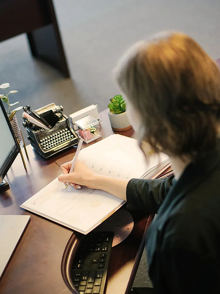 Eine Frau macht handschriftliche Notizen an einem Schreibtisch im Büro.