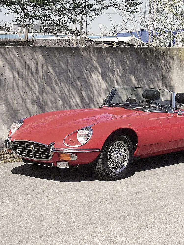 Ein roter Jaguar E-Type steht in der Sonne vor einer Mauer