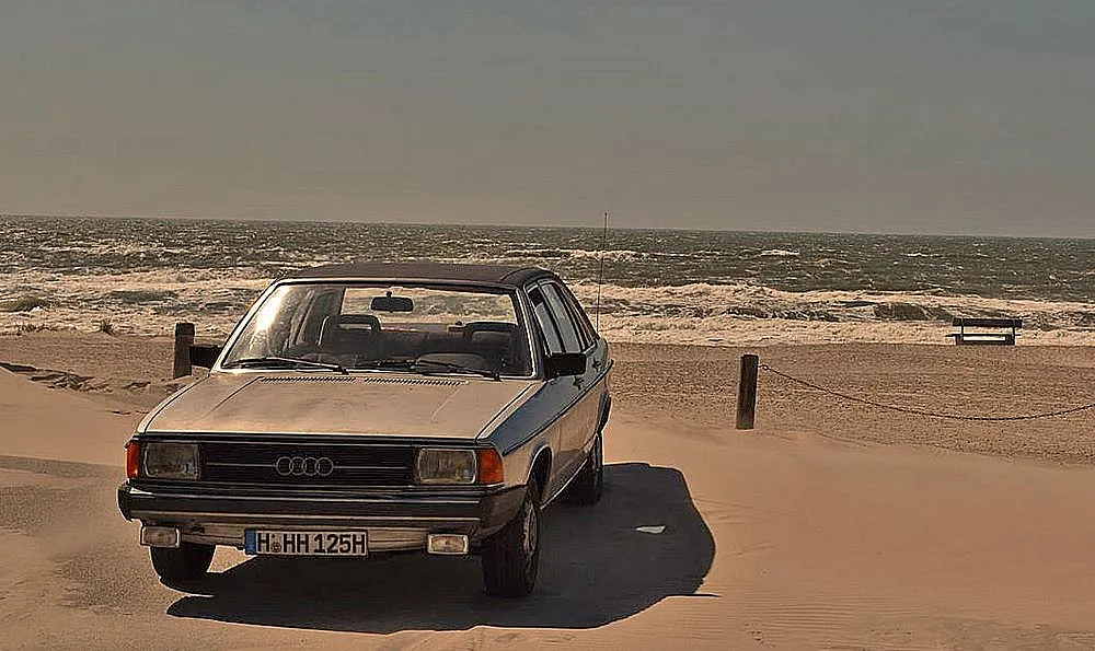 Ein Audi 100 Typ 43 steht am Strand in der Nähe des Meeres geparkt.