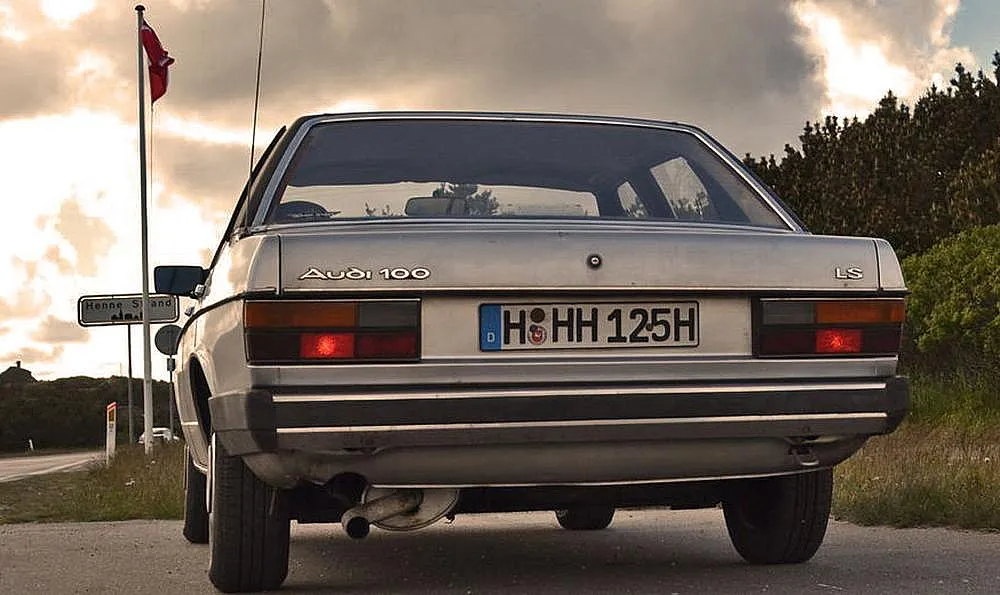 Ein parkender Audi 100 Typ 43 am Straßenrand aus der Heckansicht.