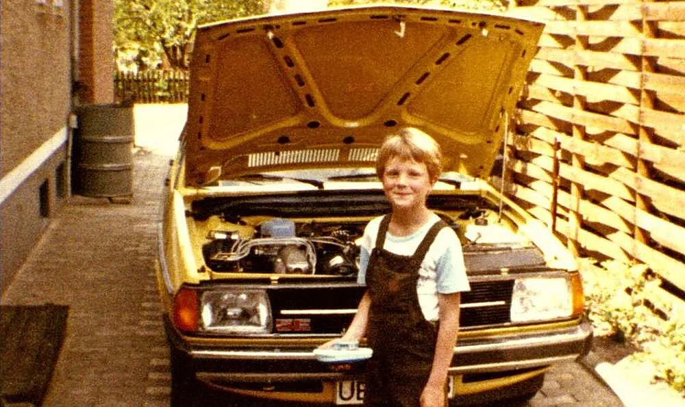 Ein Junge steht neben einem gelben Audi 100 Typ 43 mit geöffneter Motorhaube.