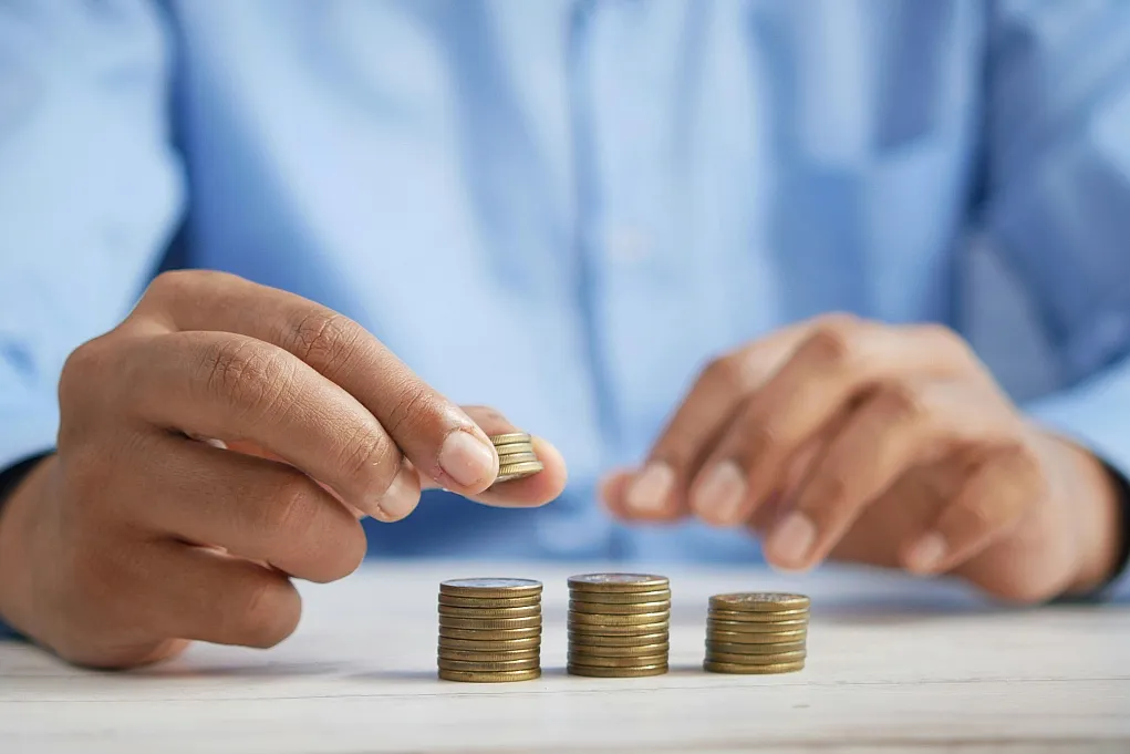Fotografie zeigt Hände, die Münzen zu drei unterschiedlich hohen Stapeln auf einem Tisch sortieren, symbolisiert Geldmanagement oder Sparen. Fokus liegt auf den Münzen und Händen, Hintergrund unscharf, vermittelt Thema Finanzen und Vermögensaufbau.