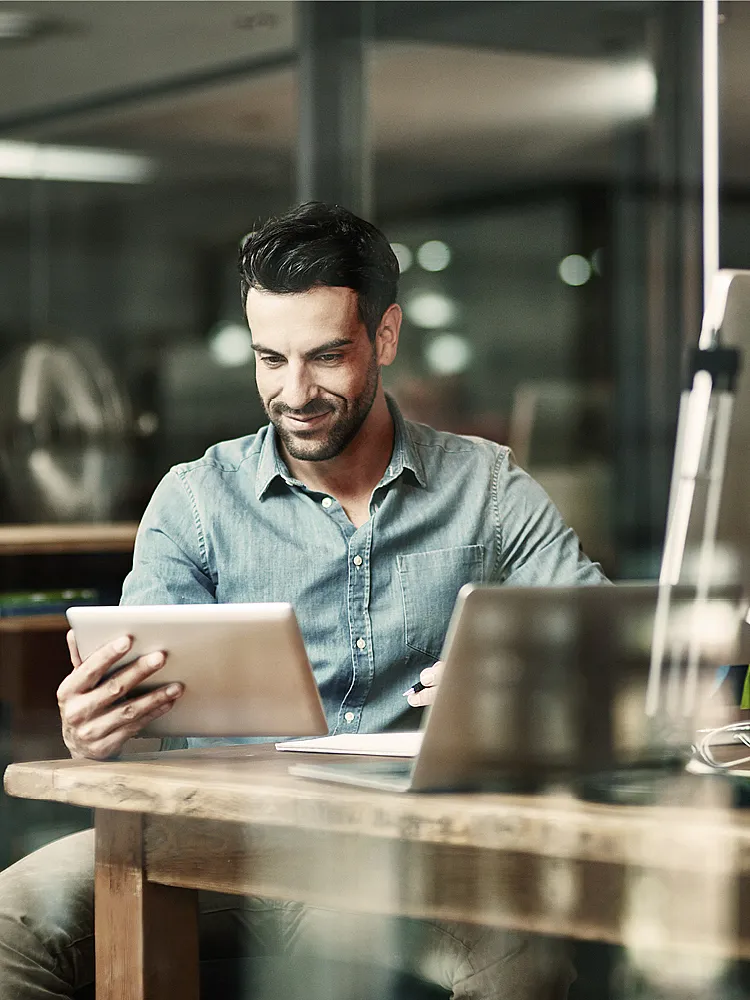 Ein Mann in blauem Hemd sitzt in einem Büro und blickt auf sein Tablet