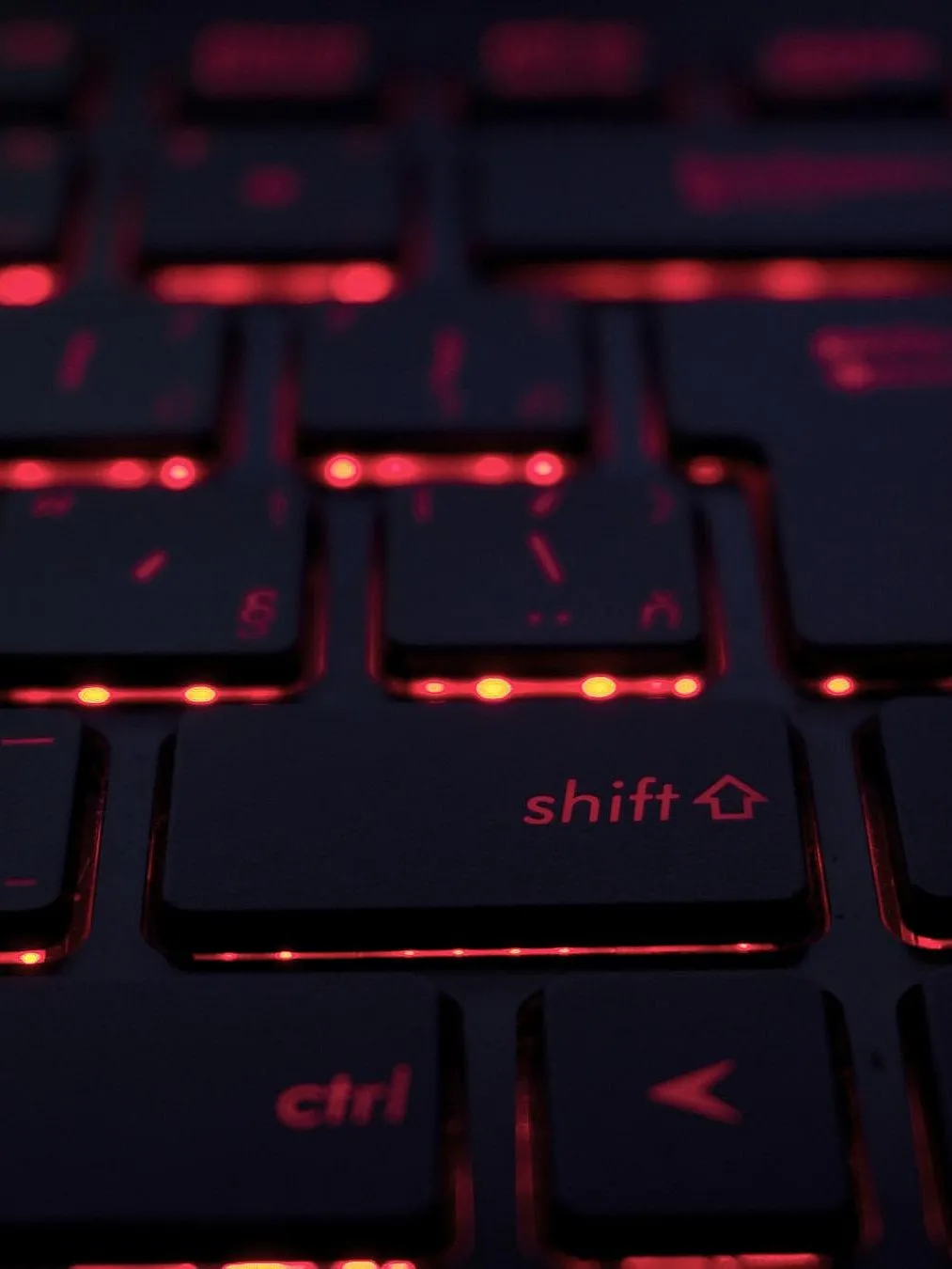 Eine Nahaufnahme einer Tastatur mit roter Hintergrundbeleuchtung. Die Tasten sind schwarz und die rote Beleuchtung scheint durch die Buchstaben und Symbole auf den Tasten hindurch.