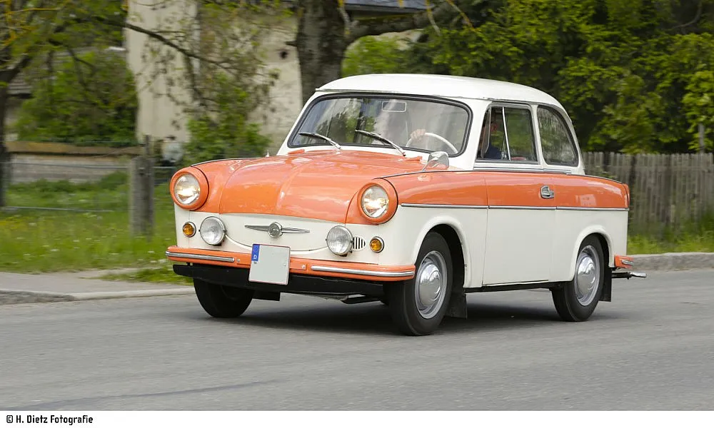 Der Oldtimer Trabant 600 in Orange und Weiß fährt die Straße entlang.
