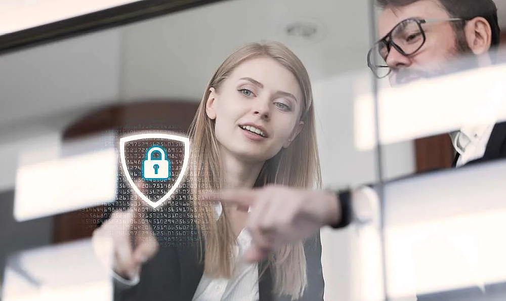 Zwei Personen in Geschäftskleidung betrachten ein digitales Sicherheitssymbol mit einem Vorhängeschloss auf einer transparenten Oberfläche.