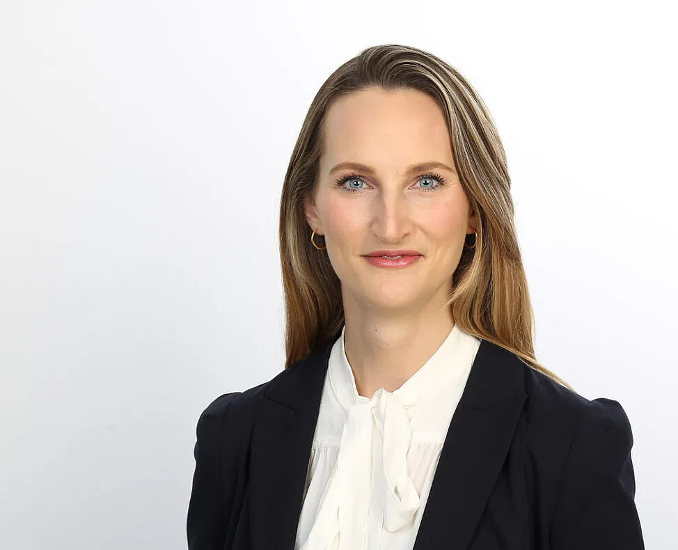 Gisa Kimmerle, eine Frau mit langen Haaren, trägt eine weiße Bluse mit einer Schleife und einen dunklen Blazer. 