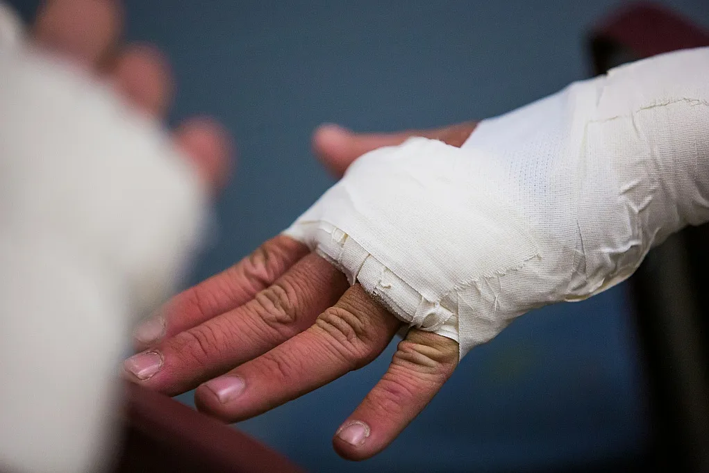 Fotografie einer Hand mit weißem Verband um Handgelenk und Finger, vermutlich zur Stabilisierung oder Schutz nach Verletzung. Fokus liegt auf detailreicher Darstellung der Bandage und entspannt ausgestreckten Fingern vor unscharfem Hintergrund.