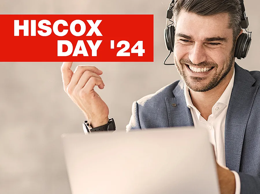 Eine Person trägt ein Headset und benutzt einen Laptop. Das Gesicht der Person ist unscharf gemacht. In der oberen linken Ecke befindet sich ein rotes Banner mit weißem Text, der "HISCOX DAY '24" lautet