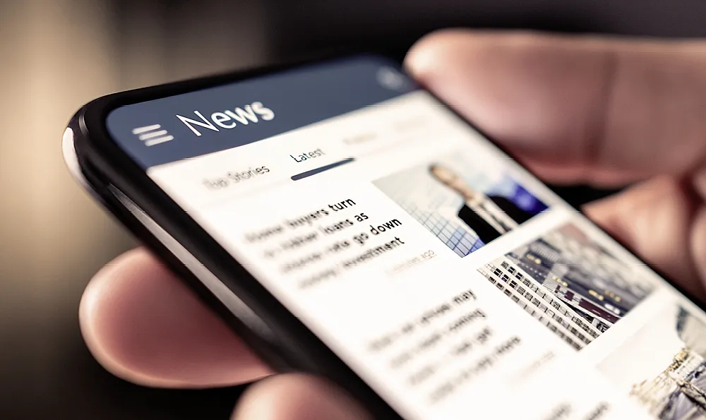 Hand hält ein Mobiles Telefon auf dem eine News-Seite geöffnet ist.