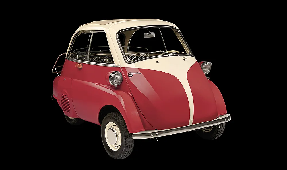 Ein klassisches Mikroauto, ein BMW Isetta, mit roter Karosserie und weißen Akzenten. Es hat eine nach vorne öffnende Tür und kleine runde Scheinwerfer.