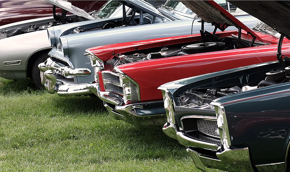 Vier Oldtimer mit offenen Motorhauben parken nebeneinander auf einer grünen Wiese