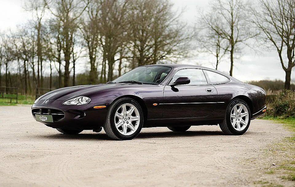 Lilafarbener Jaguar XK8 auf hellem Boden vor Bäumen, Seitenansicht