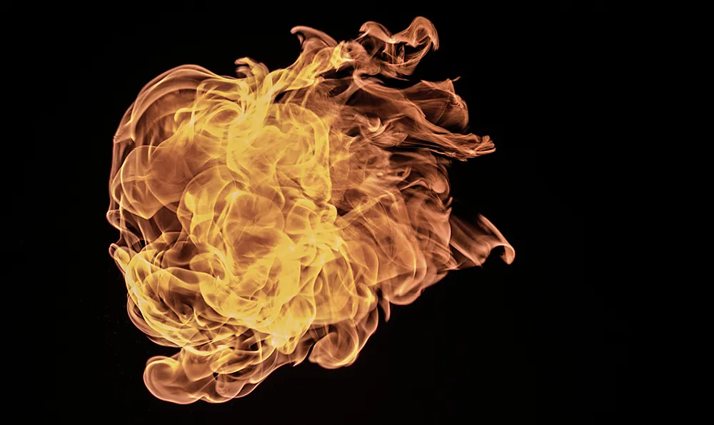 Ein dynamisches und komplexes Flammenmuster vor einem schwarzen Hintergrund. Die Flammen wirbeln und kräuseln sich, wobei sie verschiedene Gelb-, Orange- und Rottöne zeigen.
