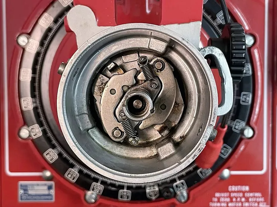  Nahaufnahme eines mechanischen Geräts mit Zahnrädern und Federn, montiert auf einem roten Hintergrund.