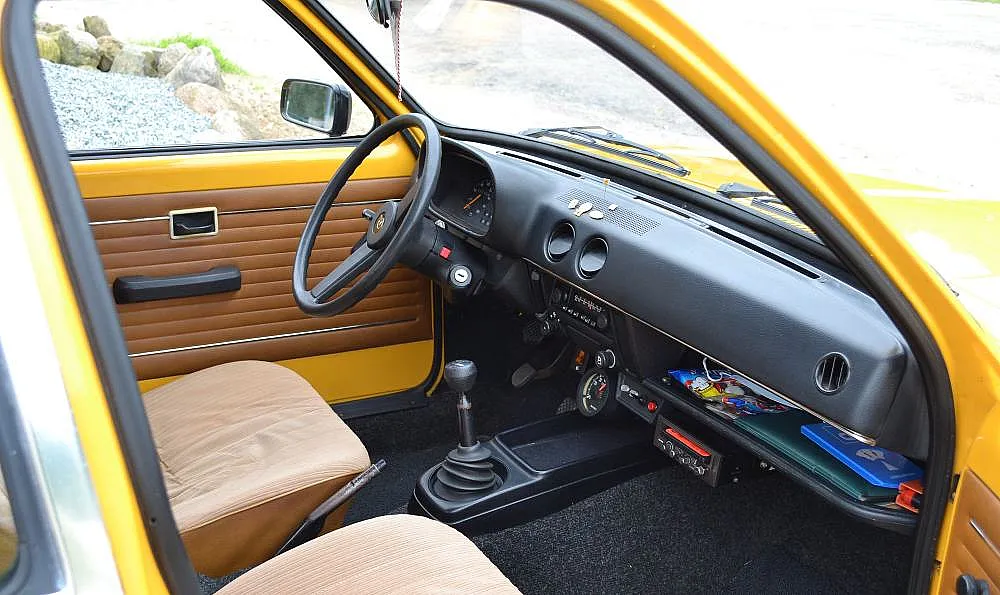 Innenraum eines gelben Oldtimers mit manueller Schaltung, drei Rundinstrumenten, Schaltern und einem alten Radio auf dem Armaturenbrett.